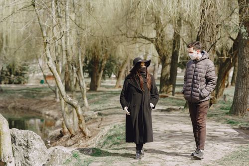 Free Full body young couple in outerwear and protective masks walking along path in empty park during COVID 19 outbreak and chatting Stock Photo