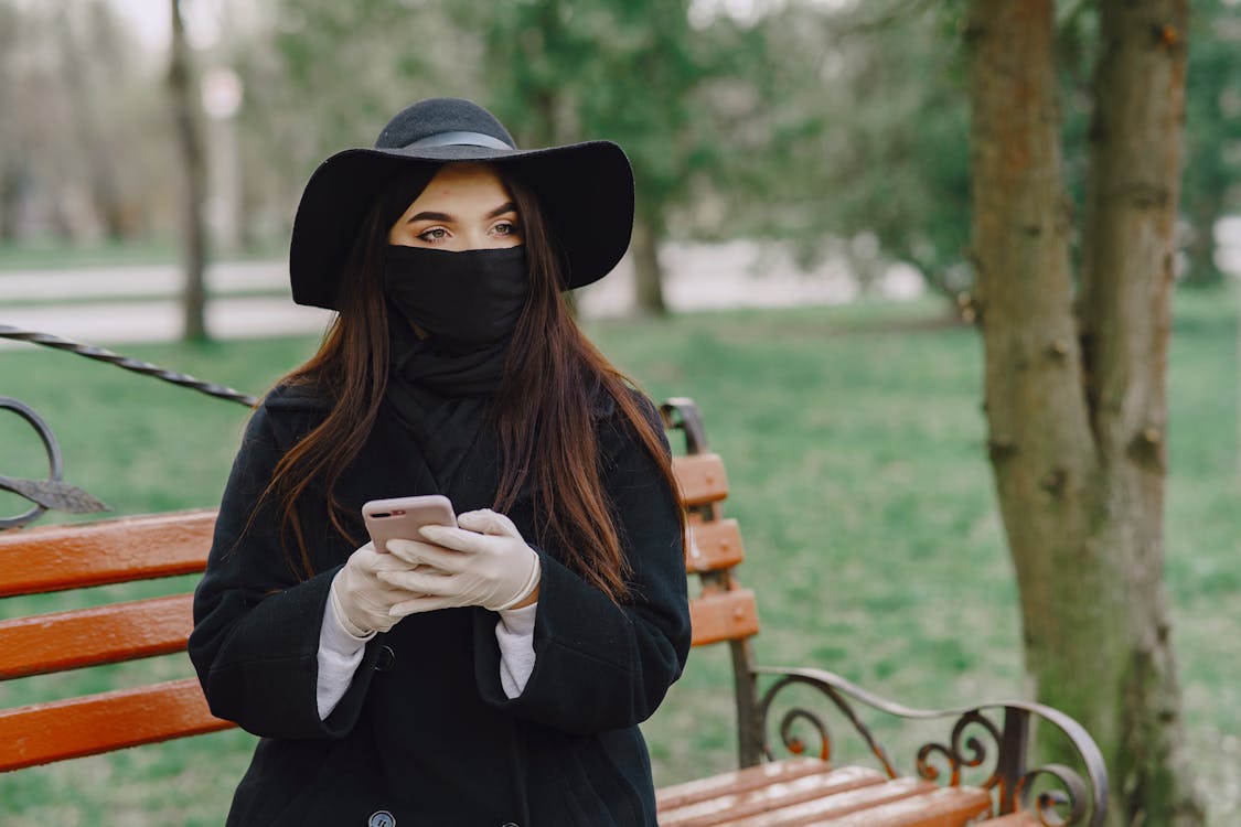 Woman in protective mask and gloves using smartphone in park