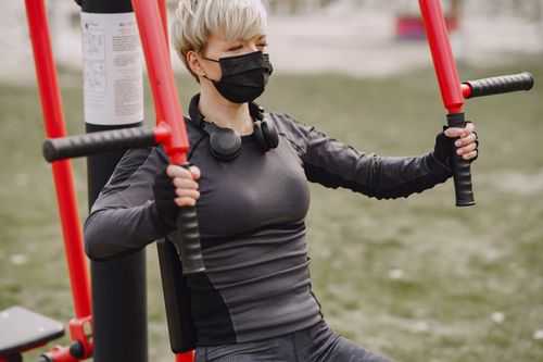 Free Strong crop sportswoman in sportswear and sport gloves wearing protective mask doing hands exercise on street workout equipment during quarantine in daytime Stock Photo