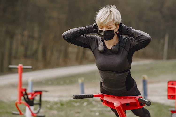 Young Woman In Protective Mask Doing Hyperextension Exercise Outdoors