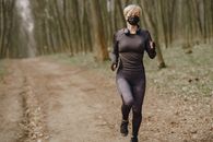 Fit woman in sportswear and mask jogging along forest alley during virus outbreak