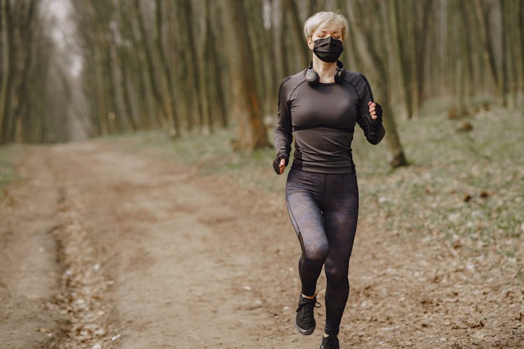 Fit Woman In Sportswear And Mask Jogging Along Forest Alley During Virus Outbreak