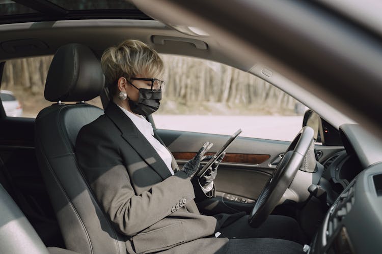 Focused Woman In Protective Mask And Gloves Using Tablet In Car