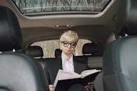 From below of concentrated female entrepreneur in elegant formal clothes sitting on backseat while reading memos in notebook riding in car