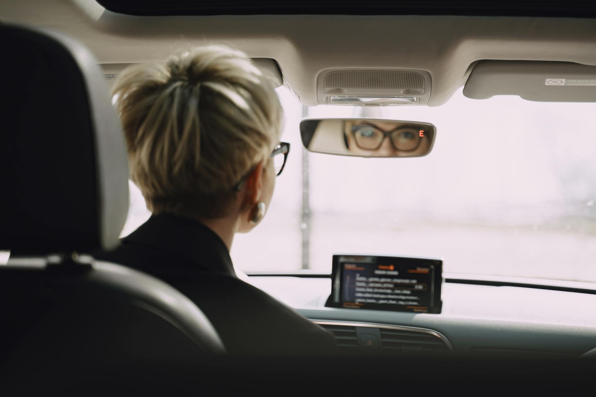 Back view of unrecognizable short hair female driver in formal clothes and eyeglasses riding car while looking at rear mirror