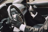 Crop person disinfecting steering wheel with antiseptic spray