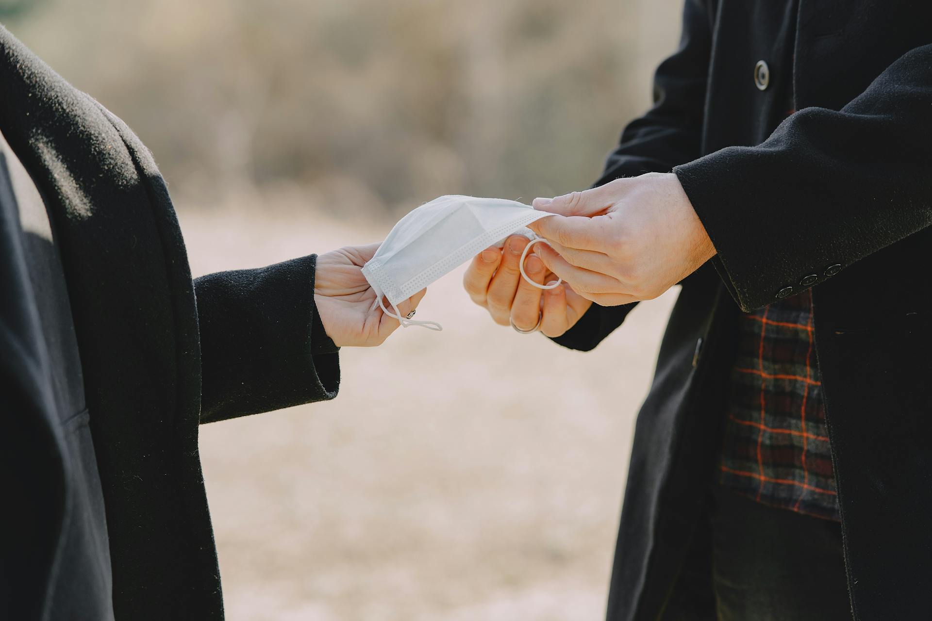 Two adults exchanging a face mask outdoors, symbolizing care and protection during a pandemic.