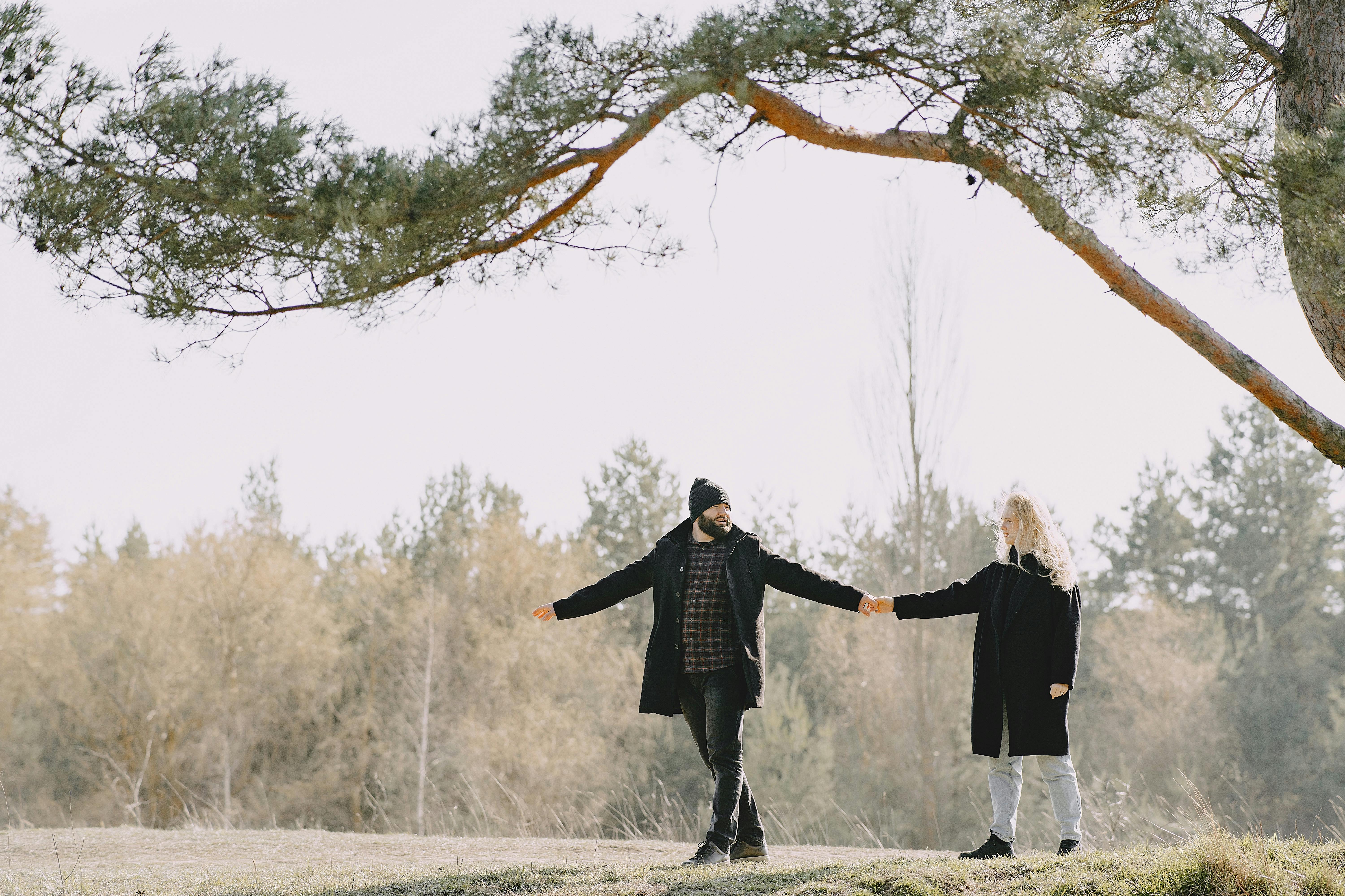 Full body of cheerful couple strolling together near tree in countryside
