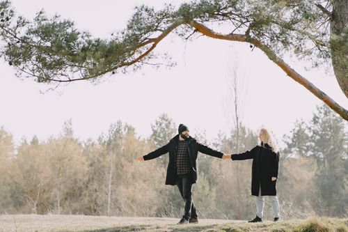Free Full body happy lovers in warm casual coats holding hands while spending time together in autumn park looking at each other Stock Photo