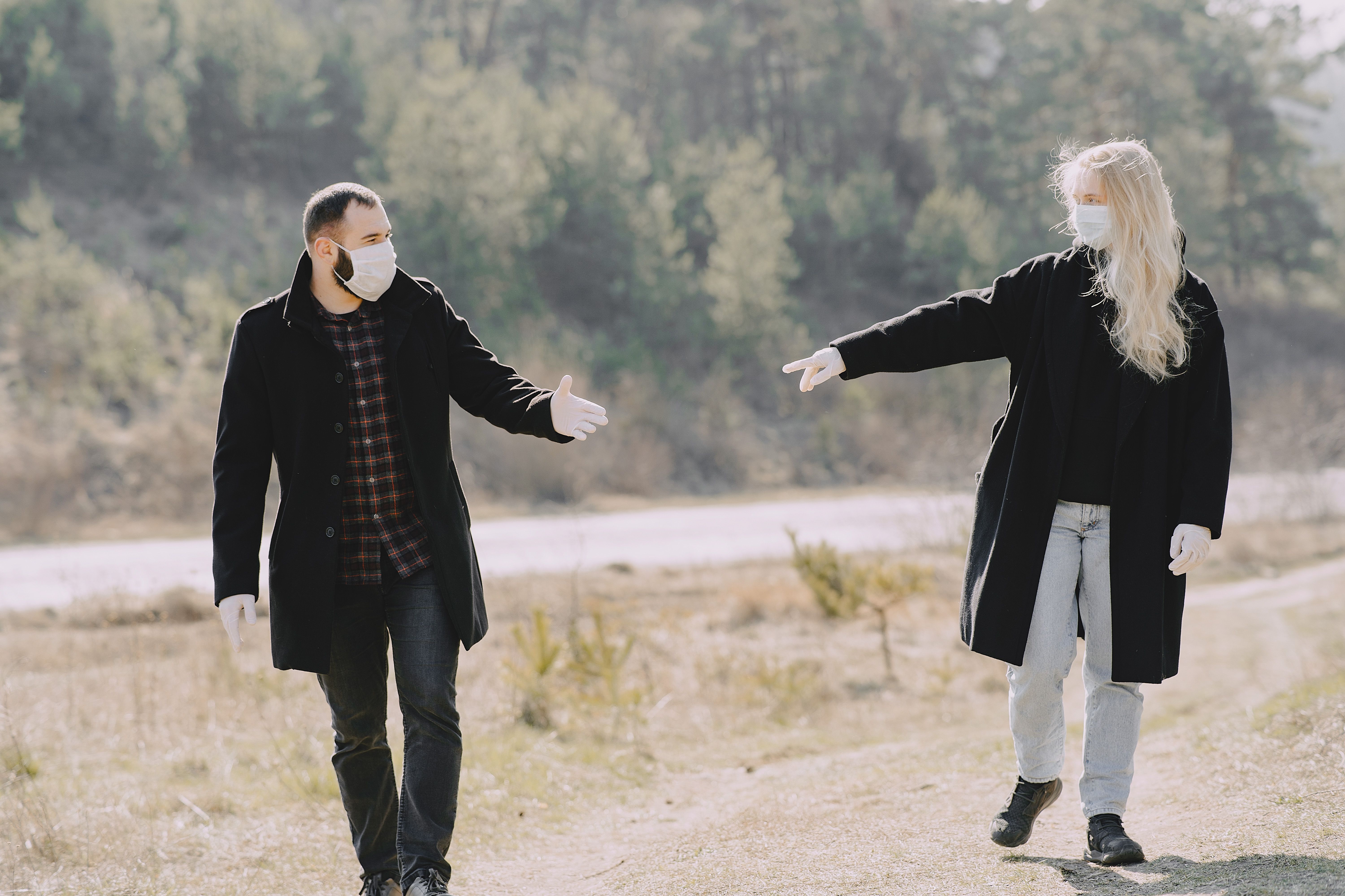 Casual couple in warm coats and protective masks latex gloves looking pulling hands to each other during weekend stroll together