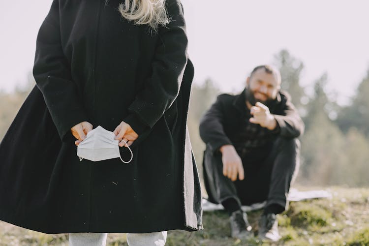 Crop Young Lady Hiding Mask From Man In Countryside