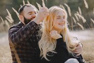 Romantic date of smiling man with closed eyes straightening hair of laughing woman while having picnic in countryside happy couple