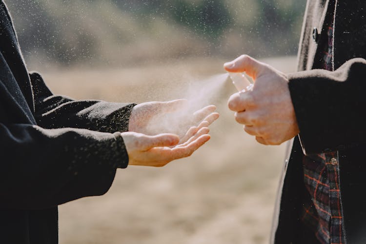 Unrecognizable Couple Sanitizing Hands With Spray