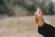 Unrecognizable man in casual wear showing bottle with liquid and spraying water outdoors