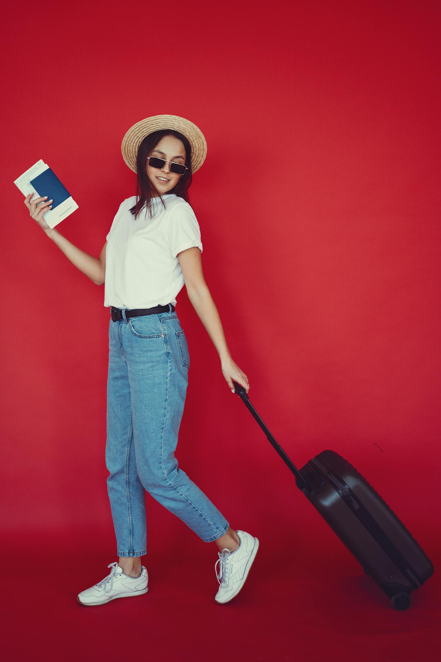 Stylish young lady walking with suitcase on red backdrop