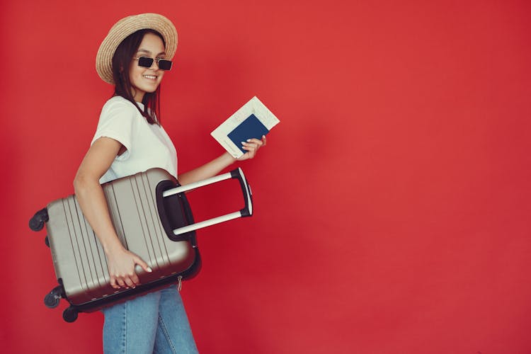 Happy Female Traveler With Suitcase On Red Background