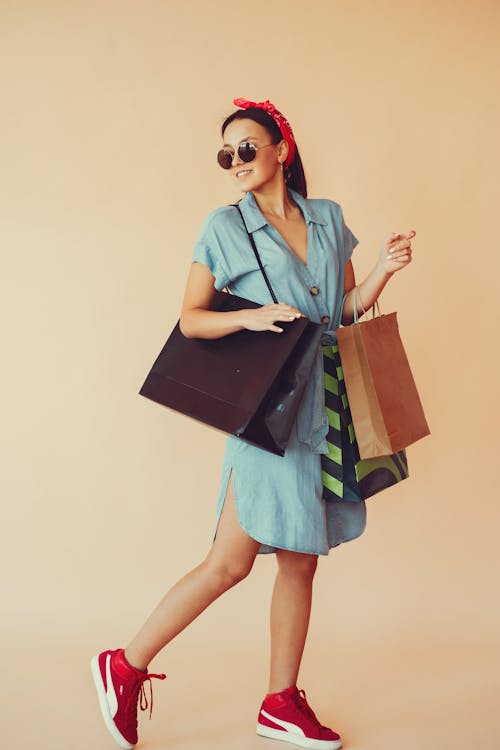 Cheerful stylish woman with paper bags on beige background