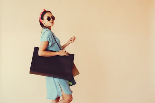 Confident young lady with shopping bags on beige background