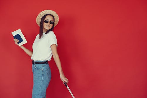 Smiling young female with luggage and passport on red background