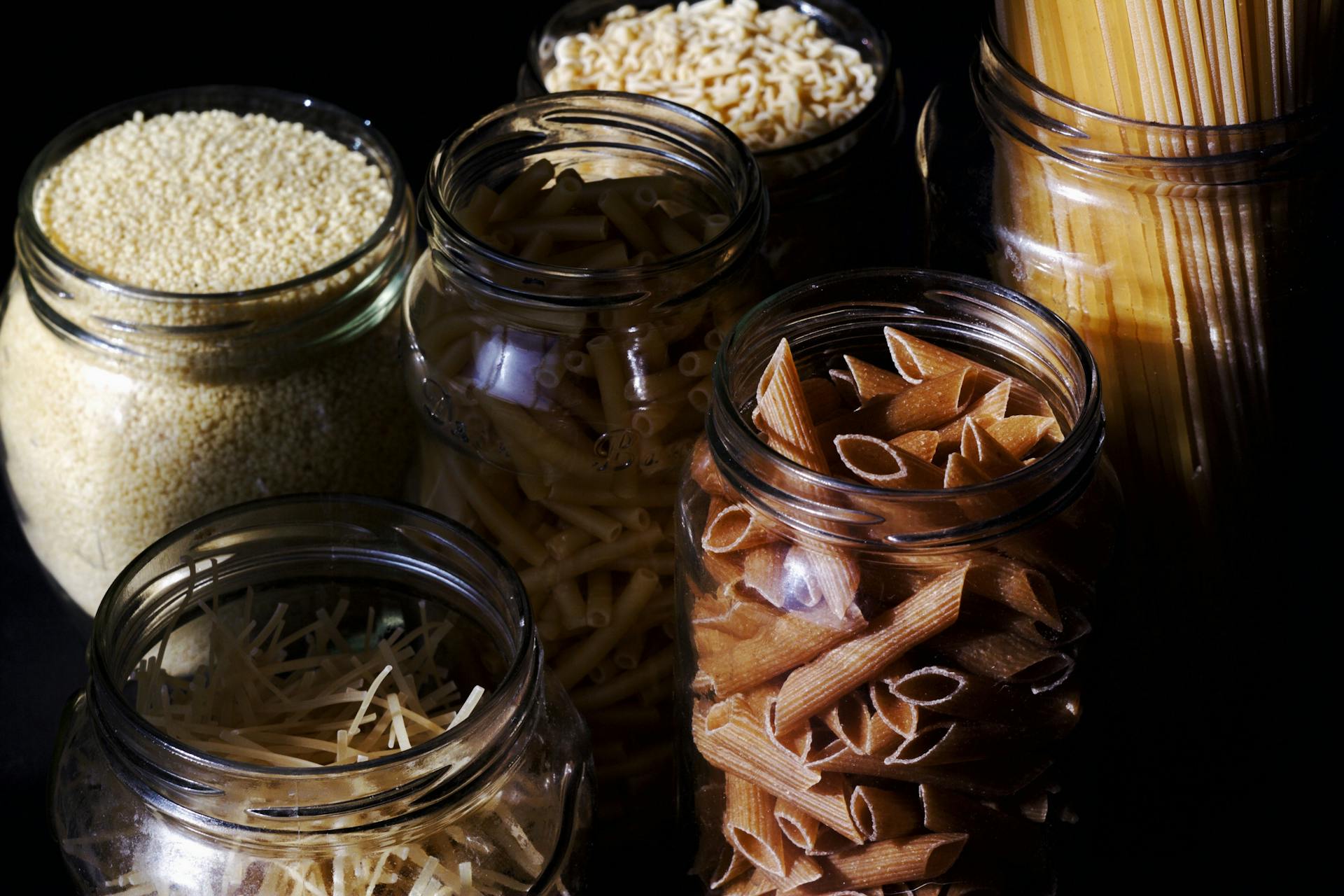 Different types of pastas and cereals in glass jars on kitchen in sunlight