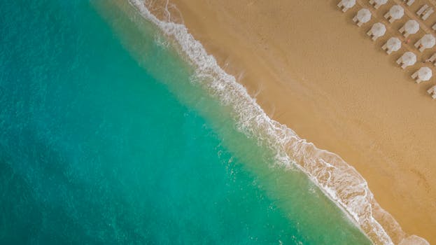 A serene aerial view of a sandy beach in Lefkada, Greece with turquoise waves and beach umbrellas.