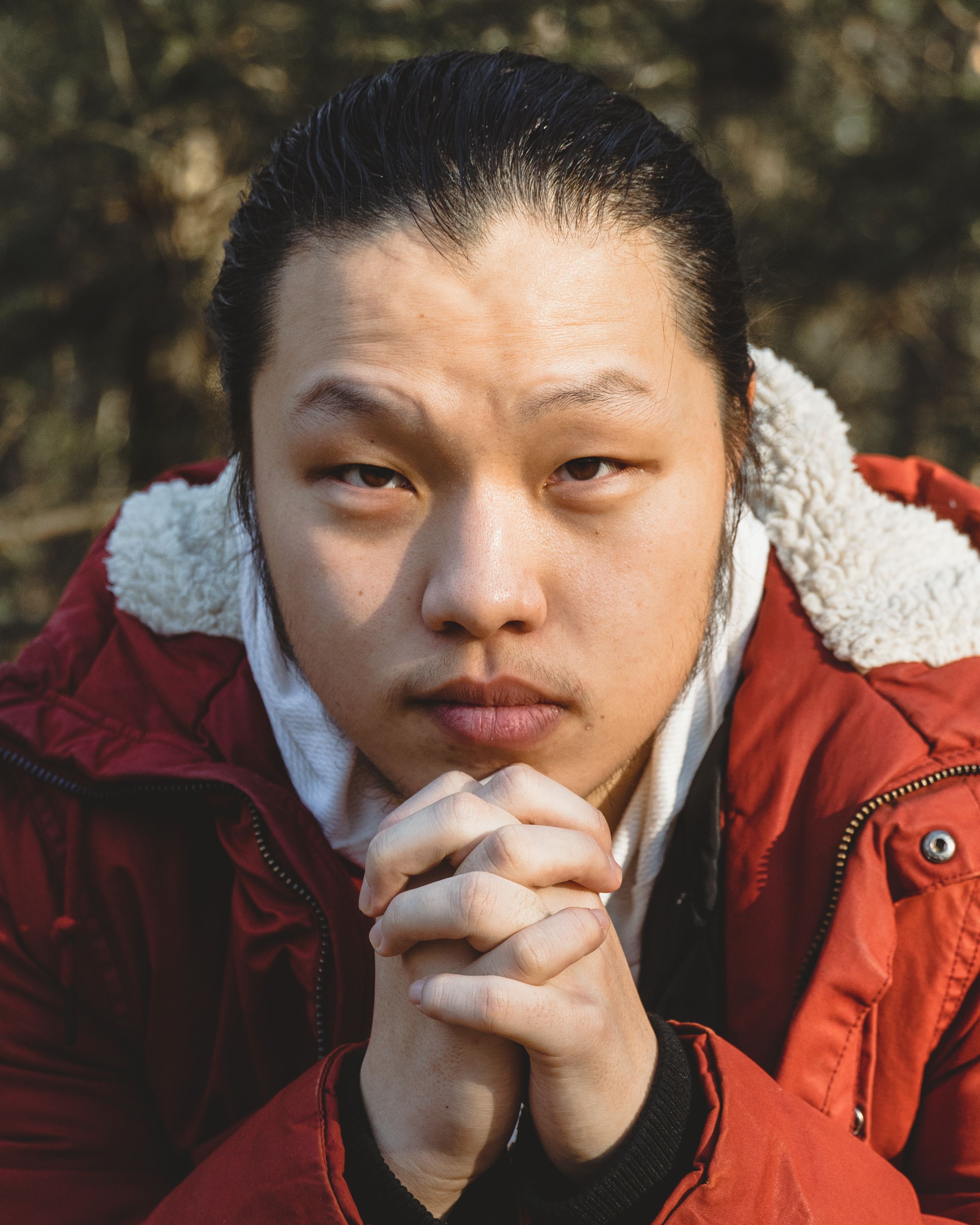 Close-up portrait of a contemplative man in a red coat with hands together.