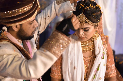 A Man Putting Accessory to a Woman Wearing Traditional Dress