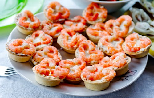 Peeled red boiled shrimps on tartlets on white plate on table in daylight in bright room