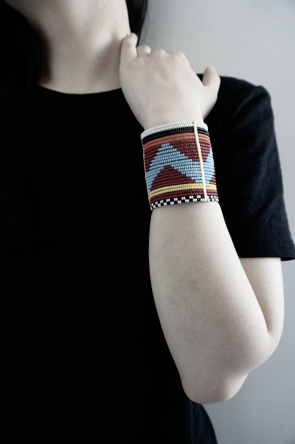 Unrecognizable young pale female in black shirt with bracelet on wrist rubbing shoulder