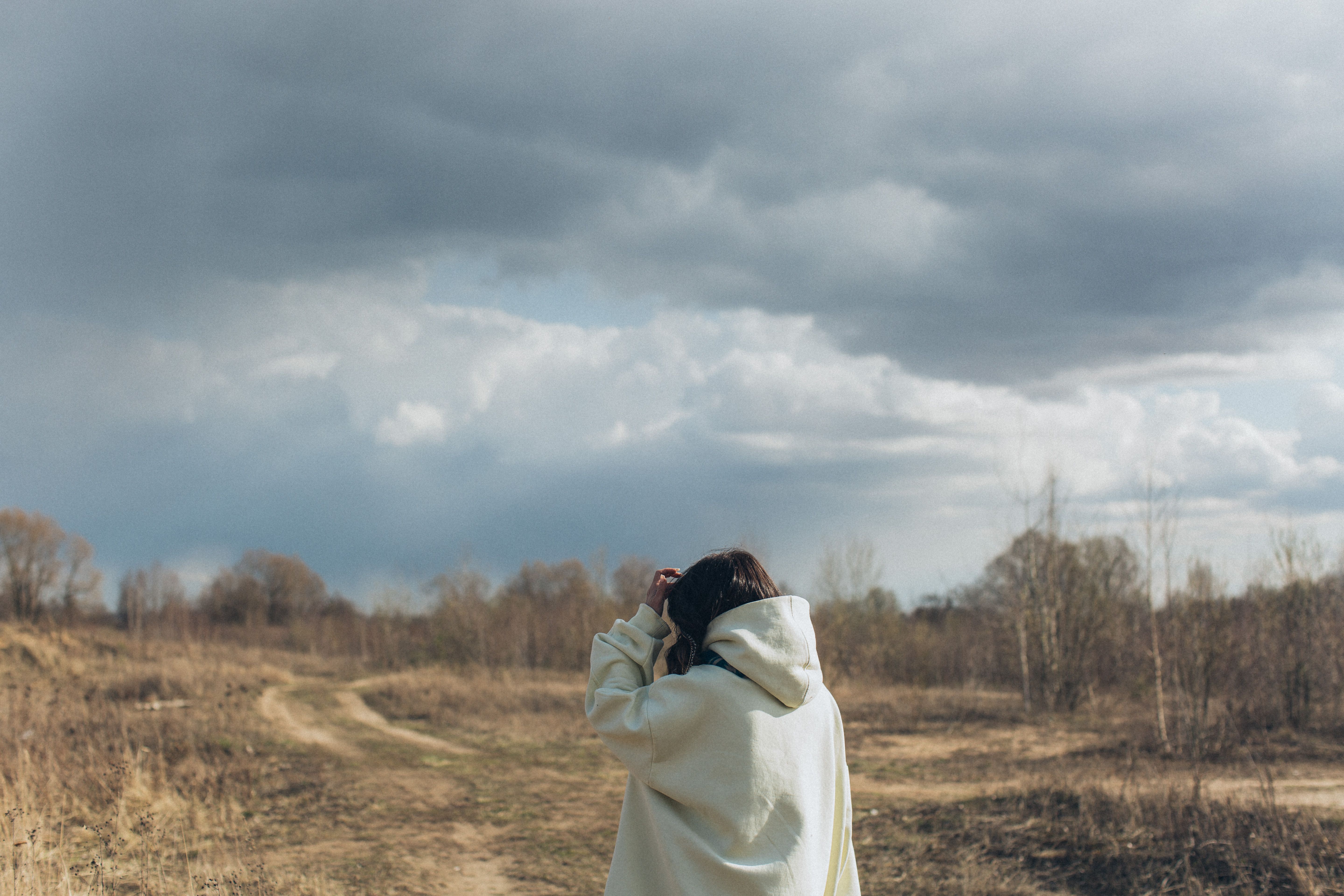 Back view of unrecognizable female in casual warm clothes walking in countryside under overcast sky
