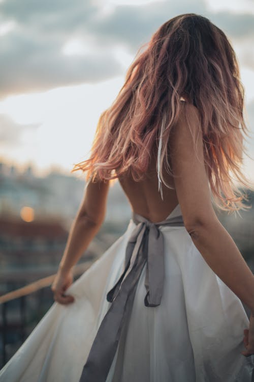Back view of anonymous female standing in delicate dress against cloudy sunset sky