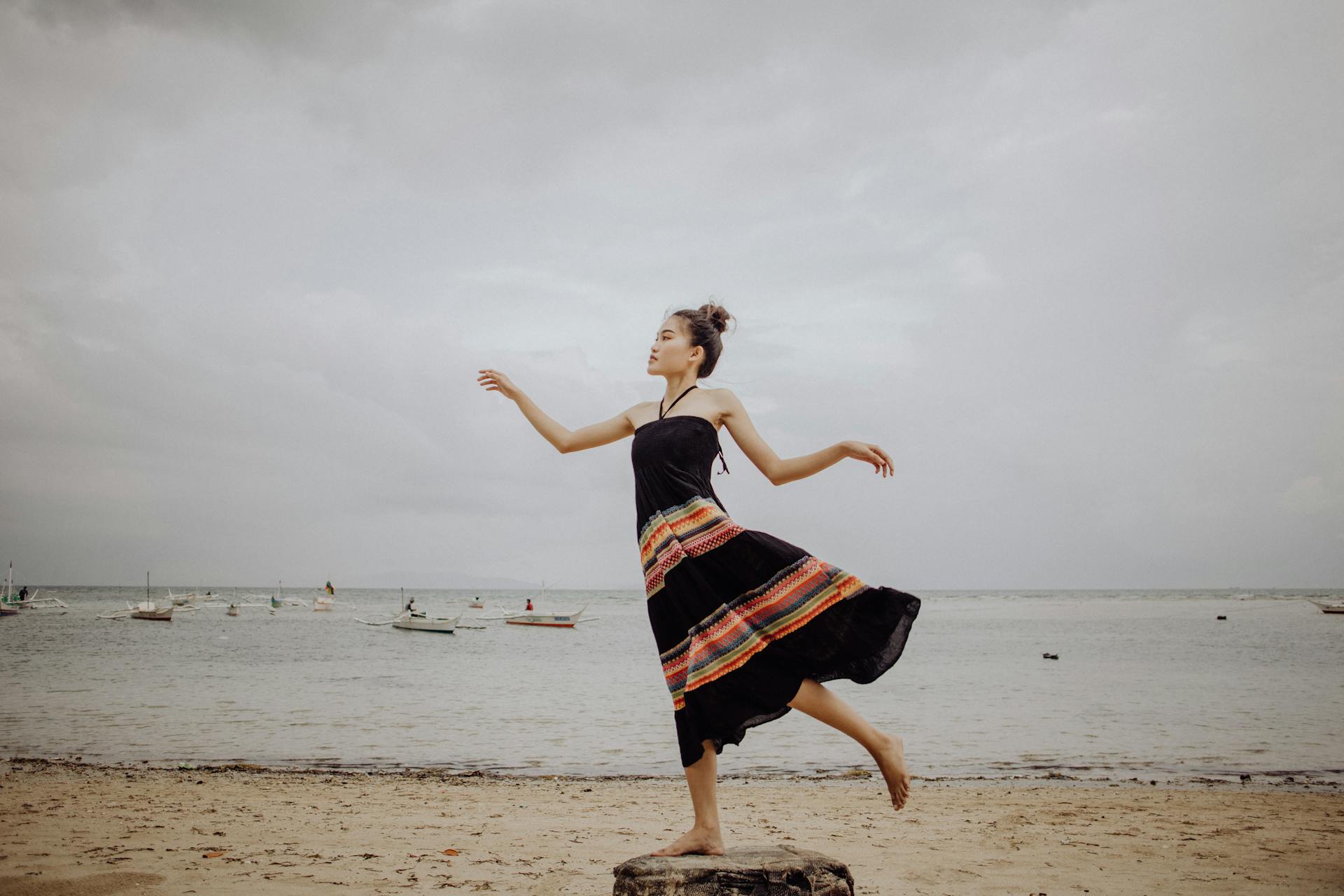 Elegant woman in a black dress posing gracefully on a Philippine beach under a cloudy sky.