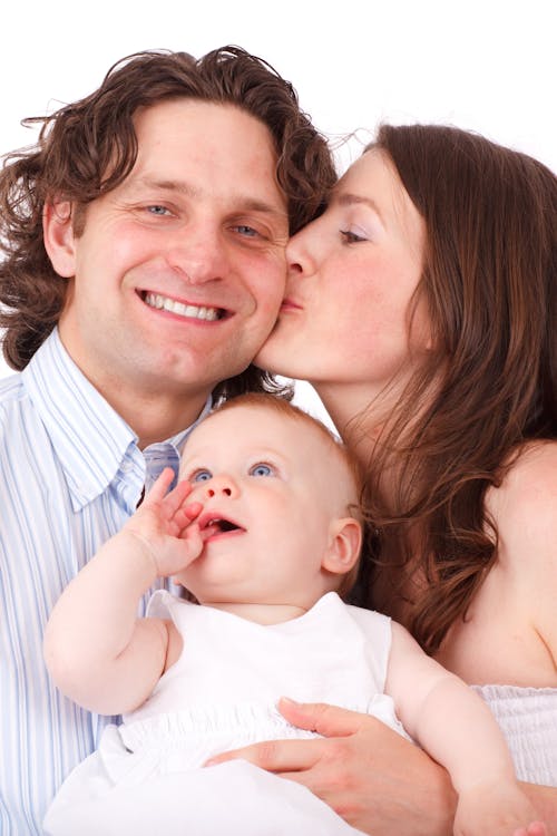 Brown Haired Woman Kissing Man in Blue White Dress Shirt Holding Baby in White Dress