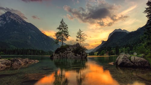 Amazing scenery of mountains and rock with trees in middle of lake with reflection of sunrise sky on water surface