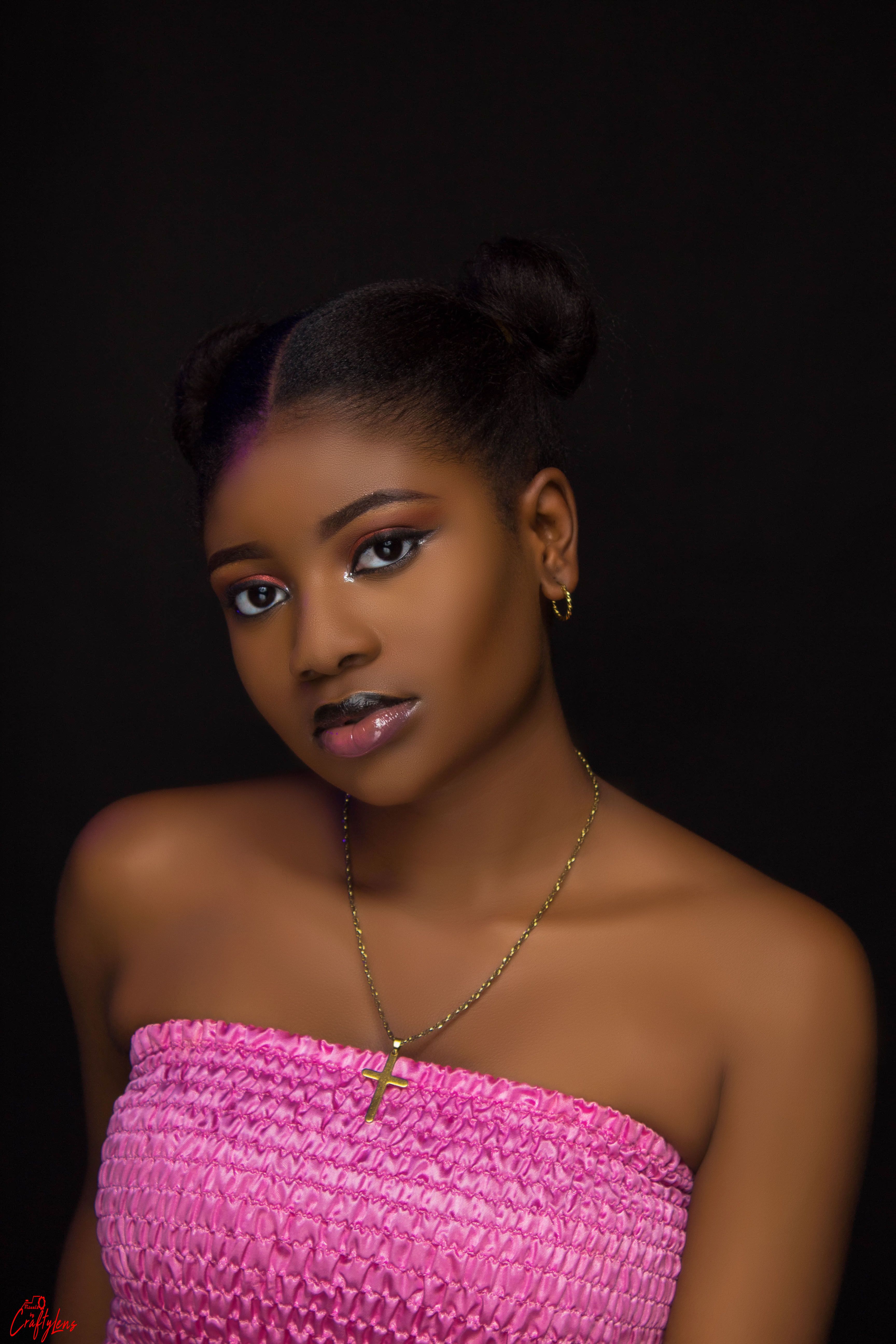 A striking portrait of a young woman against a black background, wearing a pink tube top.