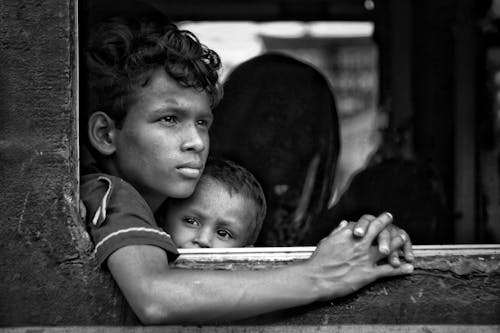 Black and white shot of calm children with mother sitting in old train near open window and looking away while going at home