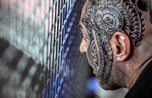 Crop ethnic man with tattoo on face near lattice