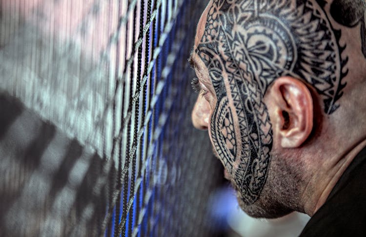 Crop Ethnic Man With Tattoo On Face Near Lattice