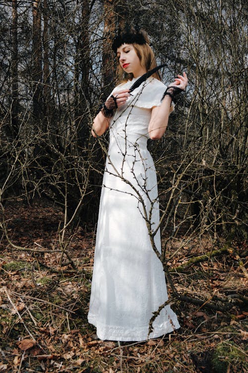 Gothic lady in white dress standing in forest