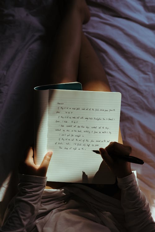 Crop lady with pen and notebook on bed at home