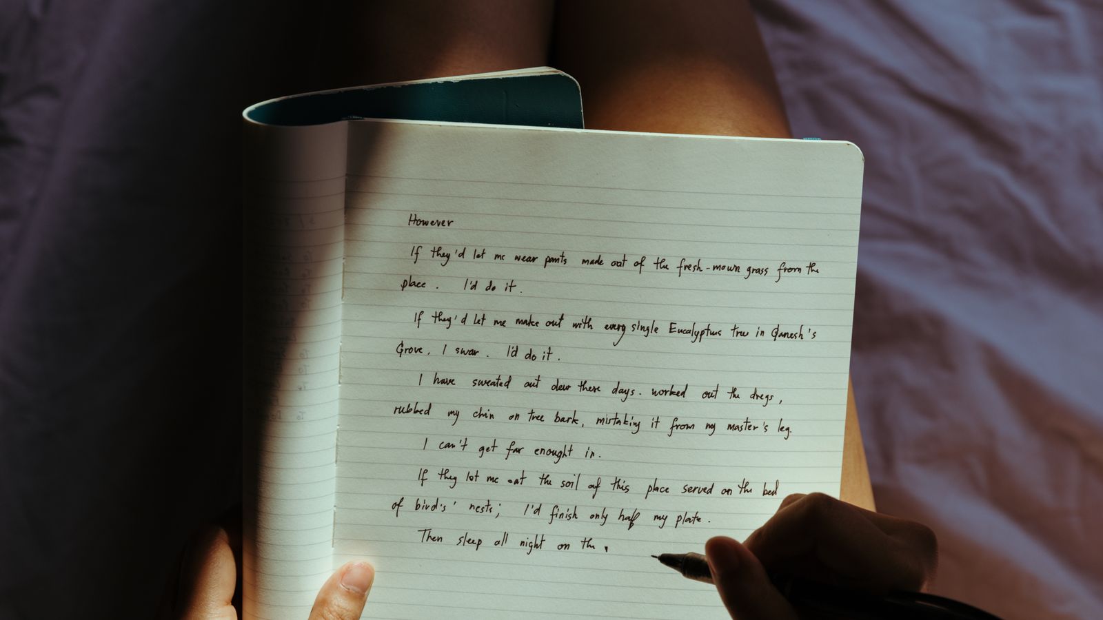 A woman writing in a notebook on a bed in a dimly lit bedroom