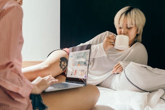 Two women relaxing in bed with coffee and laptops, embodying a calm lifestyle.