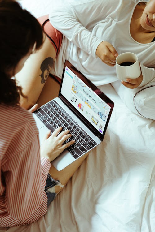 Free Woman Using a Laptop in Bed next to her Girlfriend Stock Photo