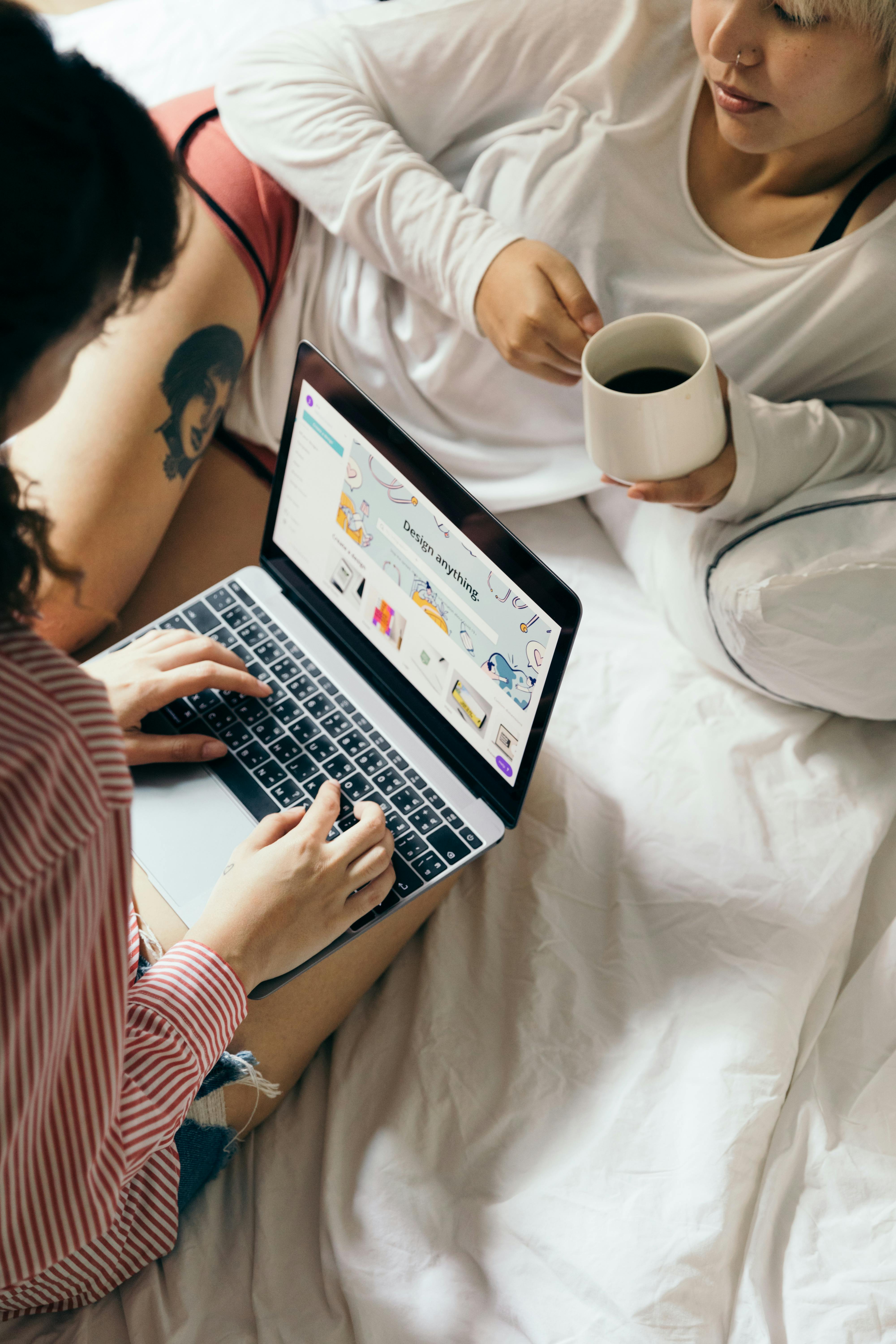 woman using a laptop in bed next to her girlfriend