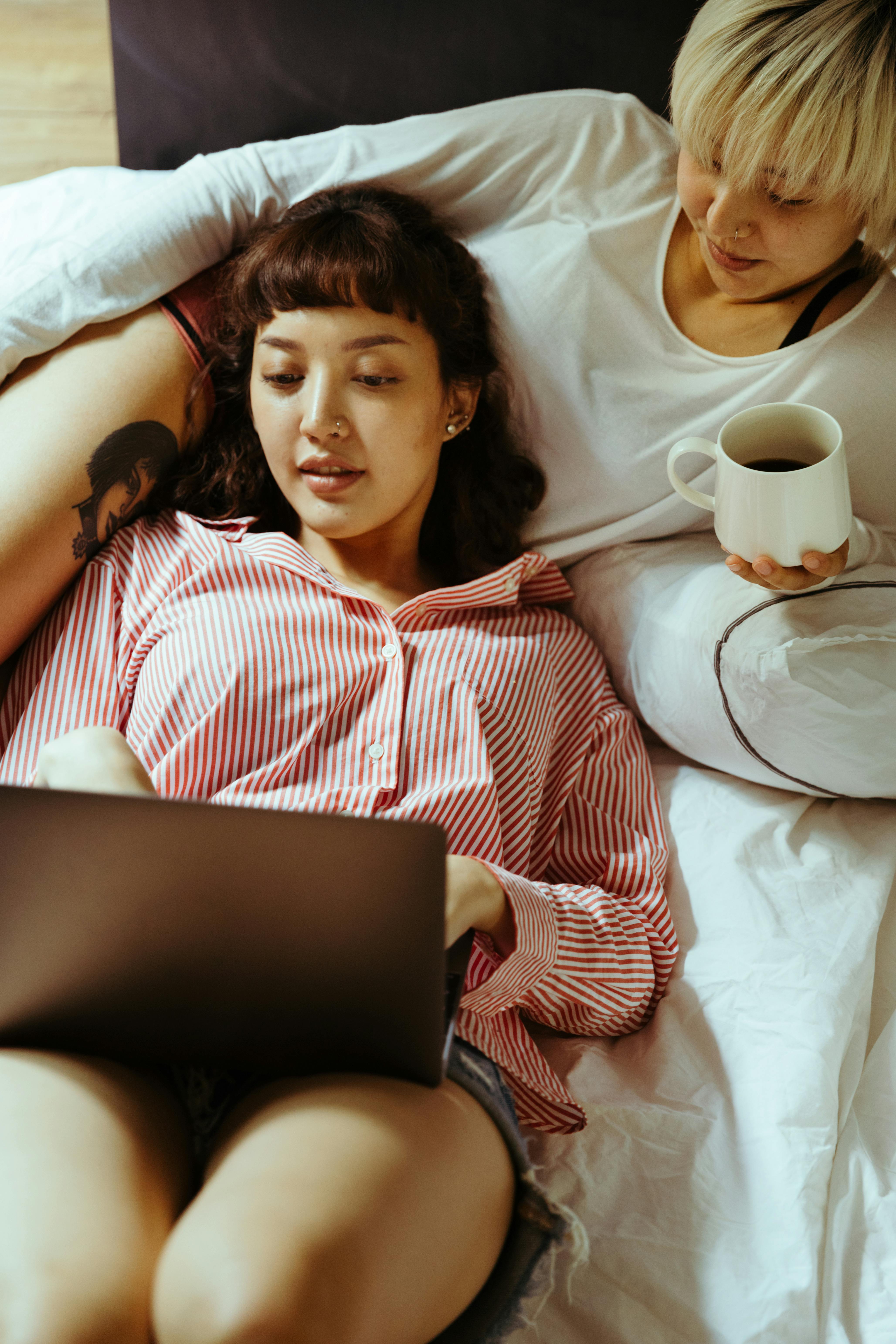 woman in bed using a laptop and reclining on her girlfriend