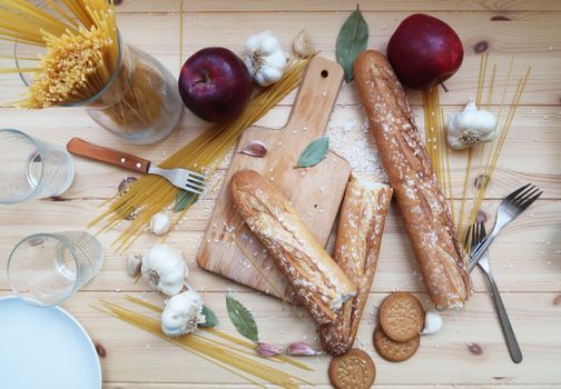 Top view of a rustic food arrangement with breads, apples, and spaghetti on a wooden table.