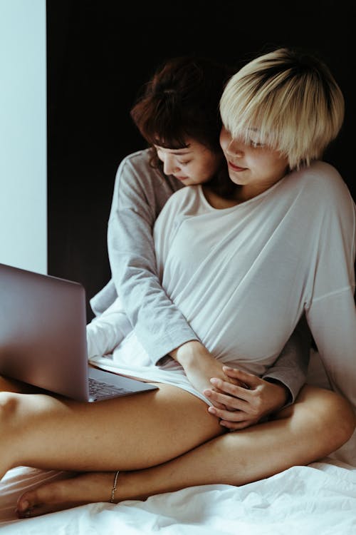 Young women lesbian lying on bed while using laptop and resting in morning together during weekend and looking at screen