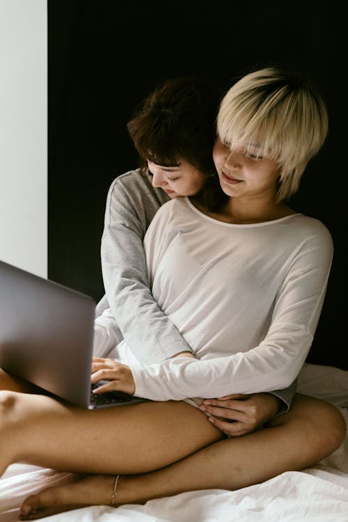 Free Loving Asian girlfriends relaxing on comfortable bed in bedroom and bonding each other while using laptop browsing internet during weekend at home Stock Photo