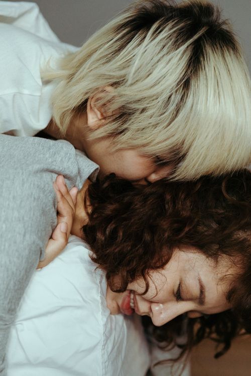 Free Side view of young women embracing each other while lying on bed and resting together during weekend time and spending time Stock Photo