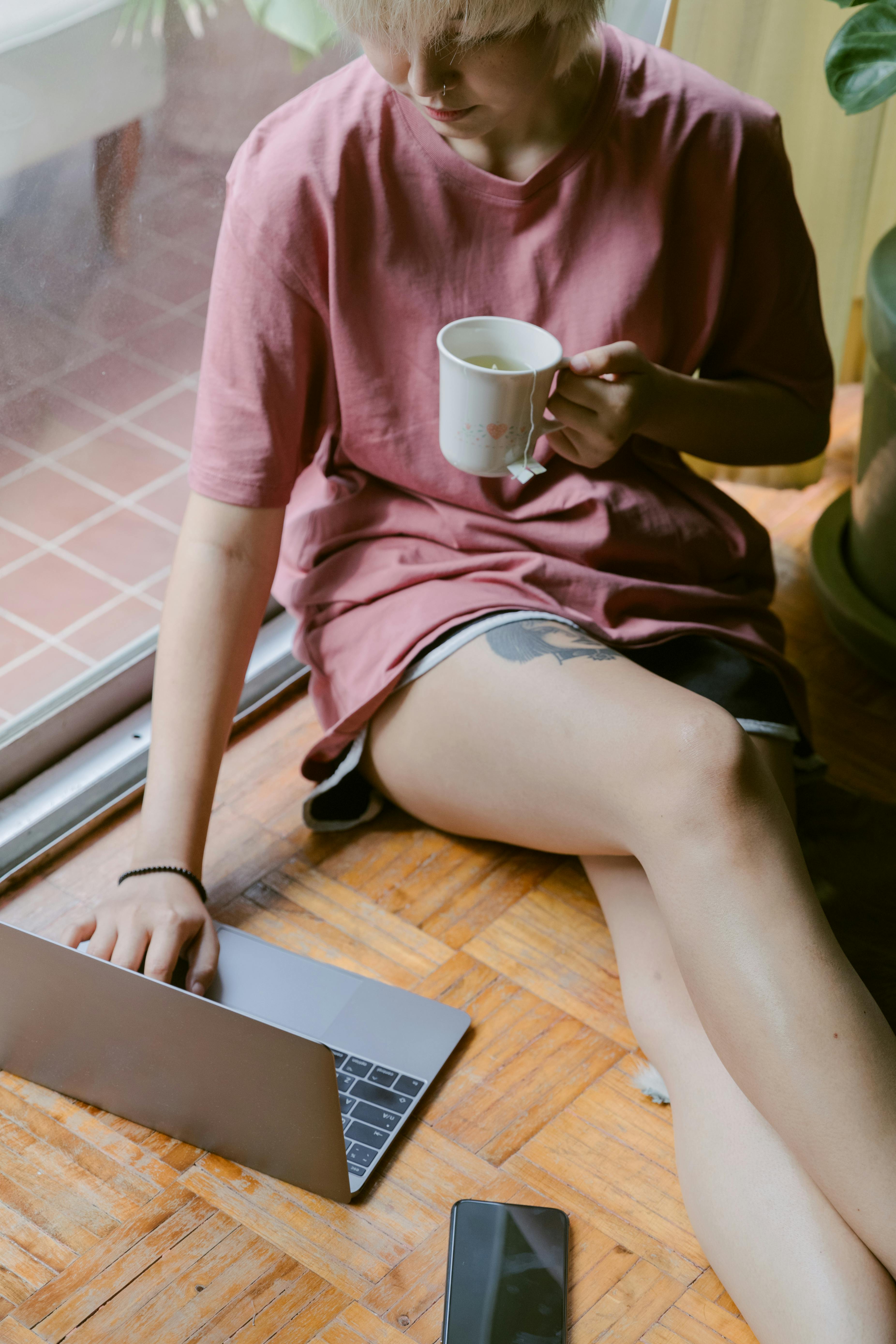 From above Asian female in morning using laptop while sitting on floor with cup of hot drink